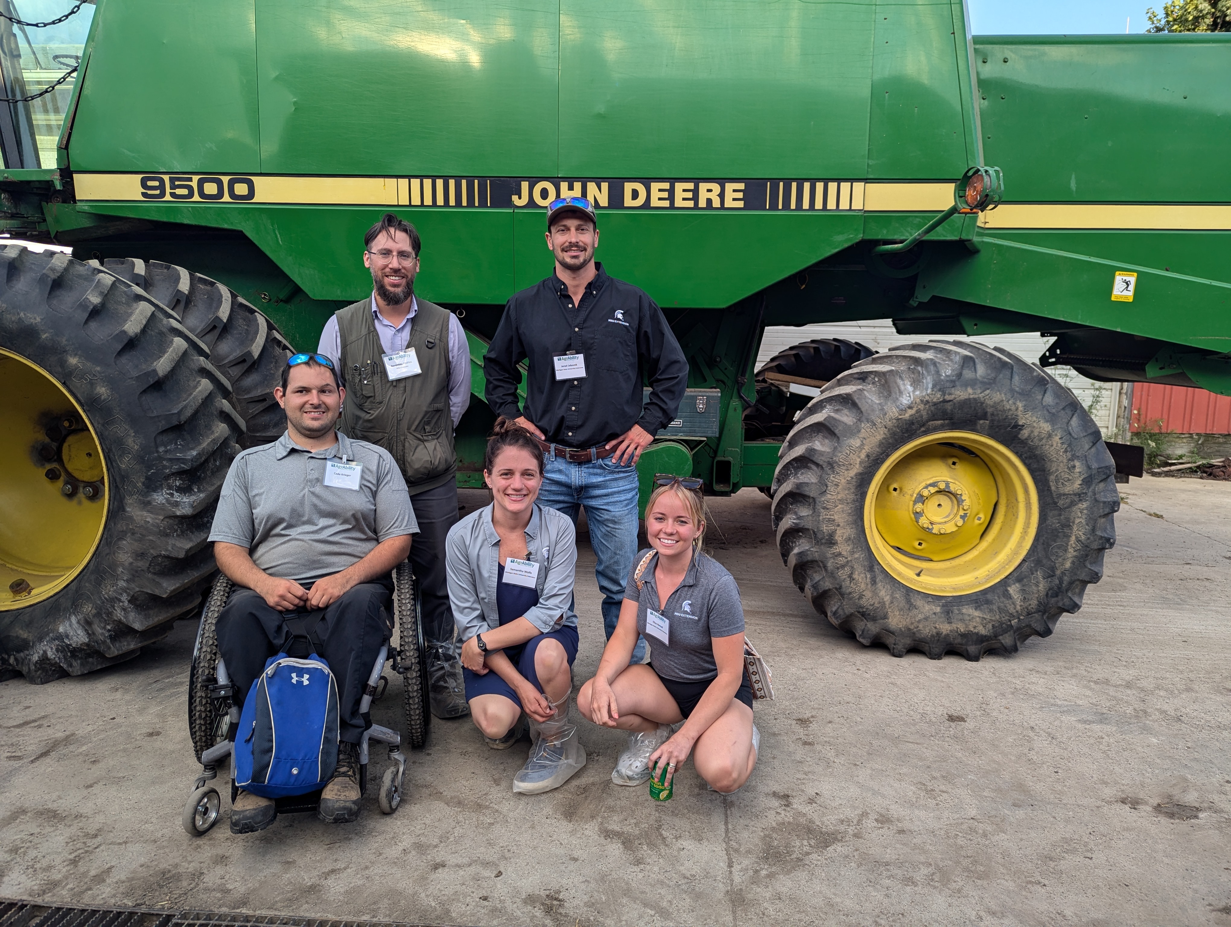 Five people posing for a photo in front of a large green piece of harvesting equipment.
